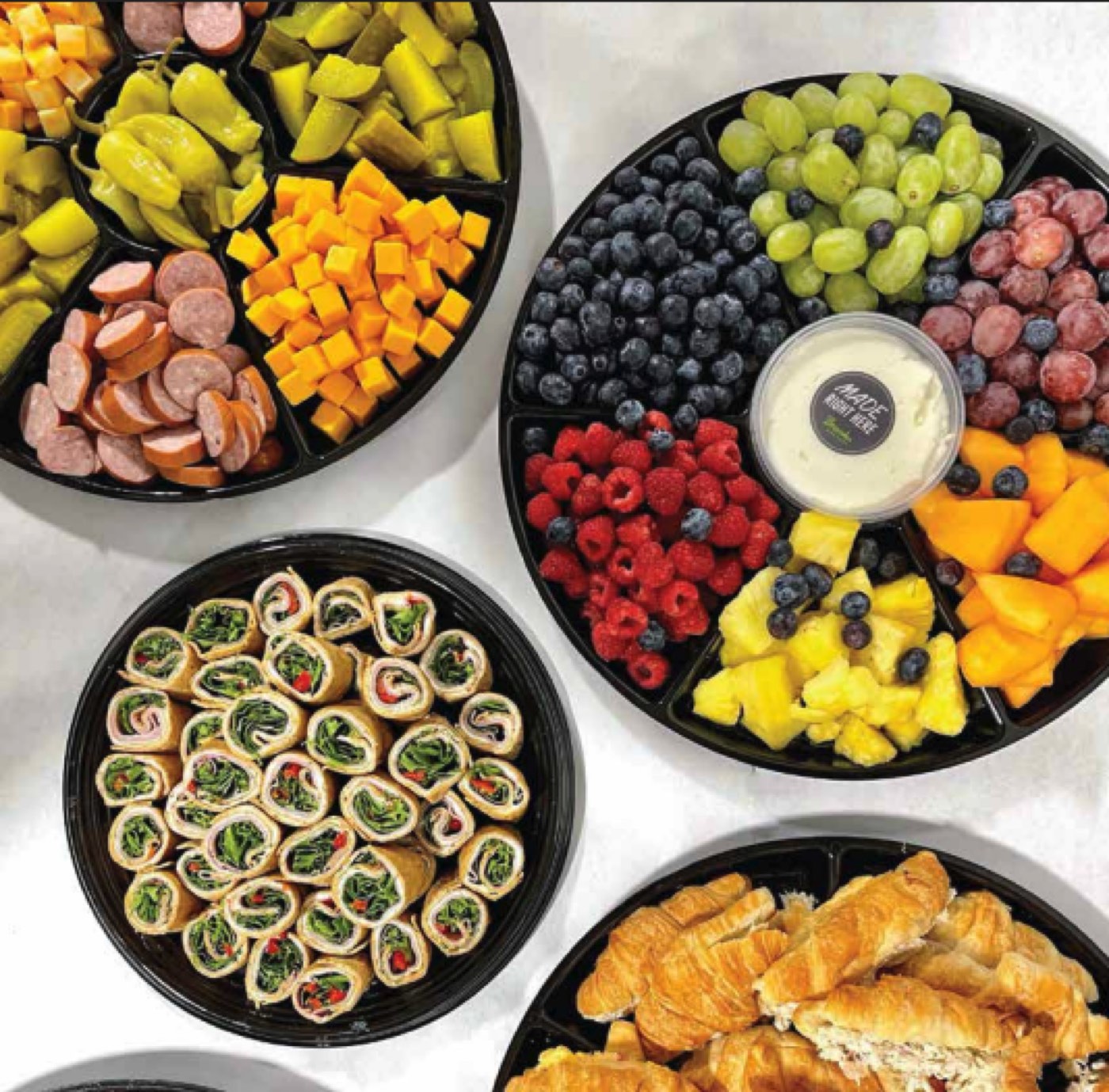 Brooks Grocery catering spread with pinwheel wraps, croissant sandwiches, and a fruit tray